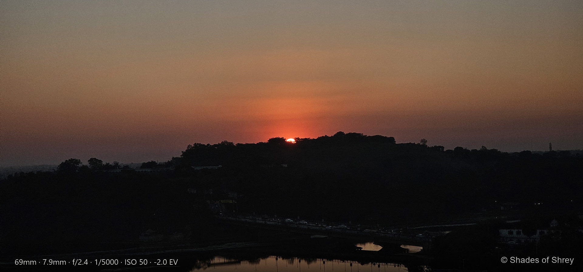 Glowing red sun setting behind dark treeline at dusk