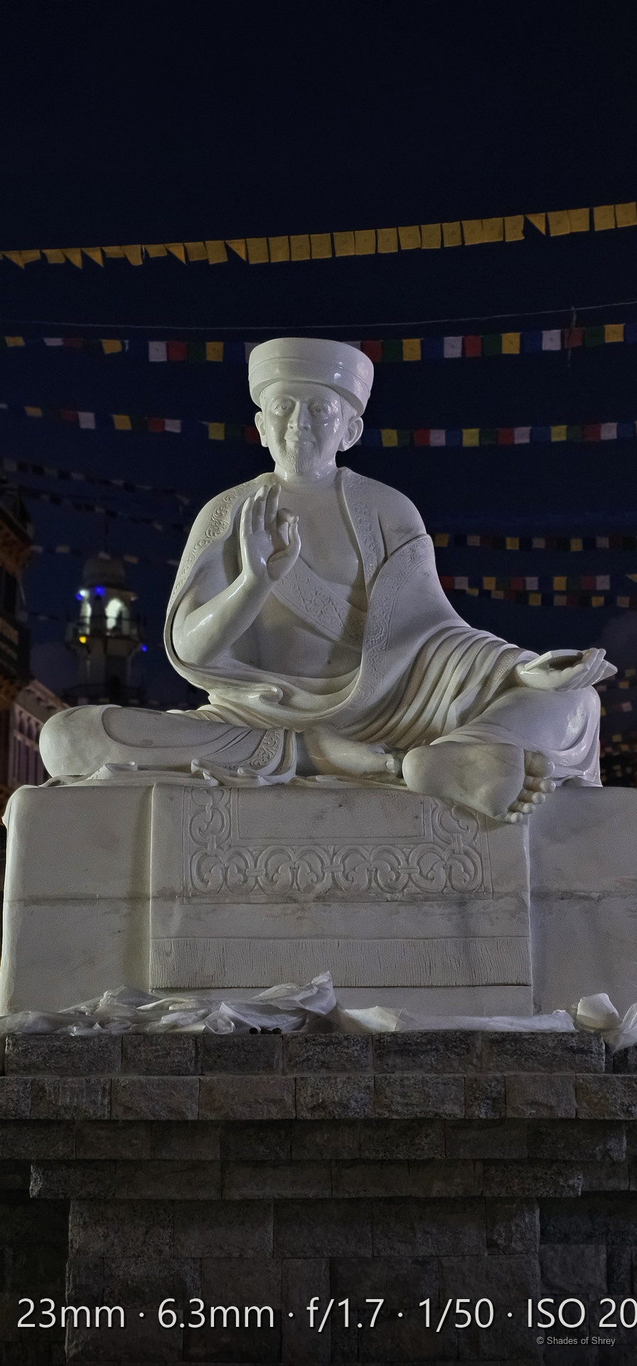 Illuminated marble Buddhist statue with prayer flags at night