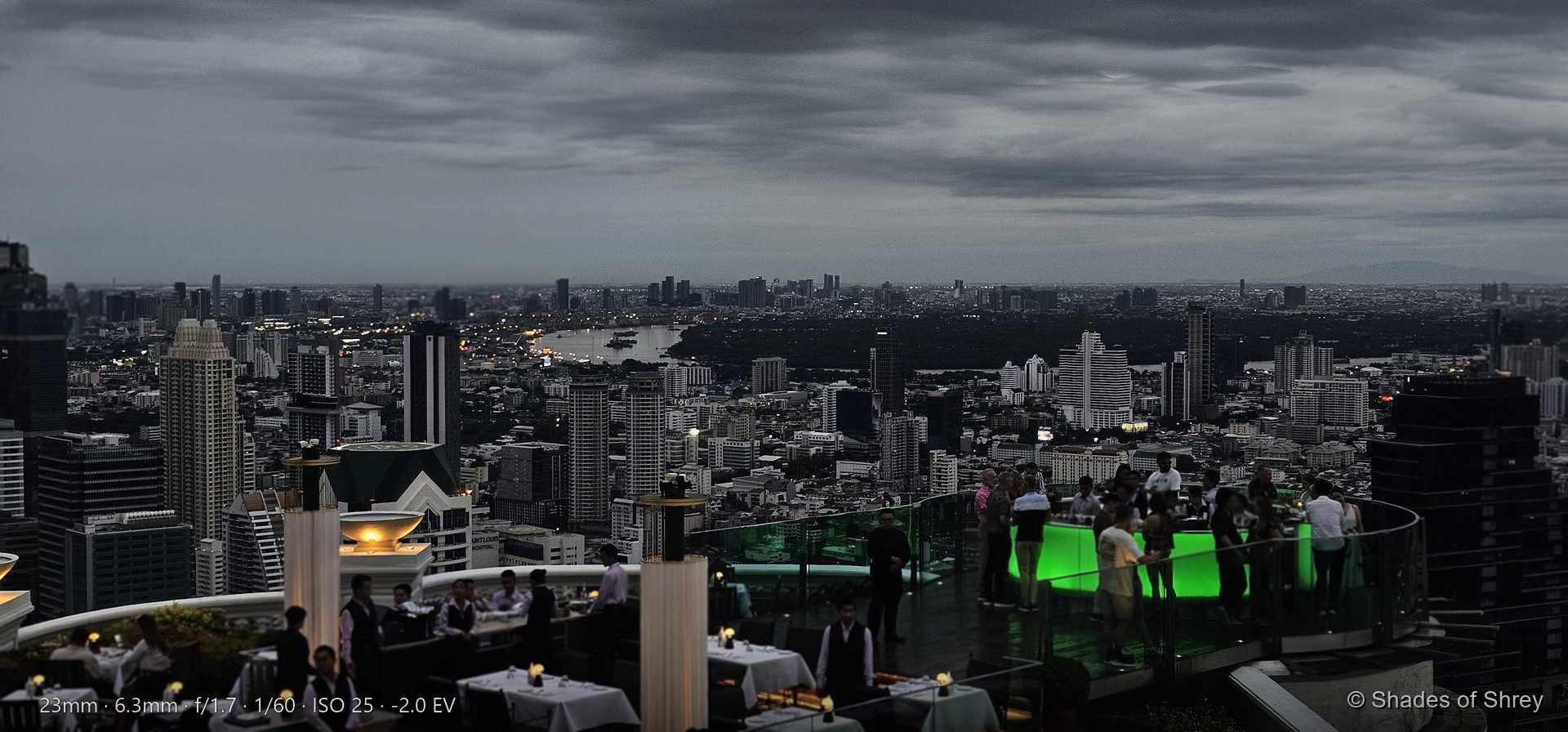 Rooftop restaurant overlooking Bangkok at dusk with emerald-green lighting
