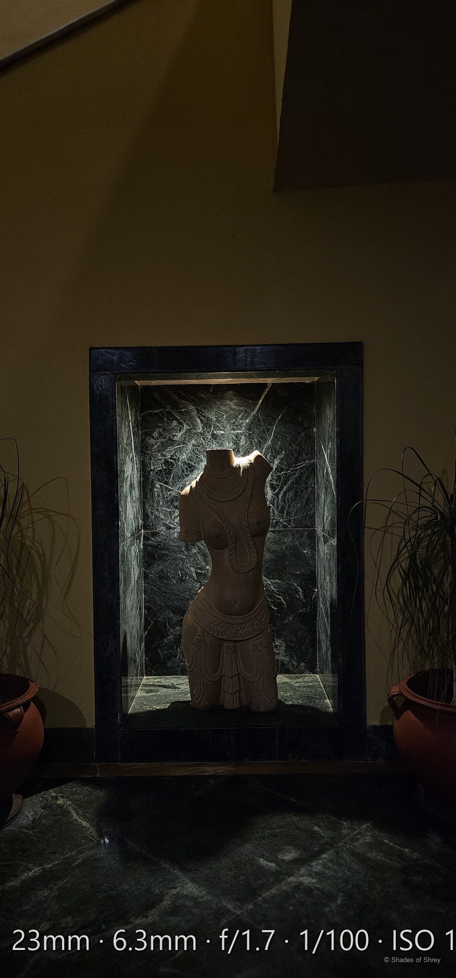 Carved wooden figure illuminated by warm light on a green marble pedestal